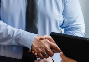 Business handshake between colleagues in a formal office meeting setting.